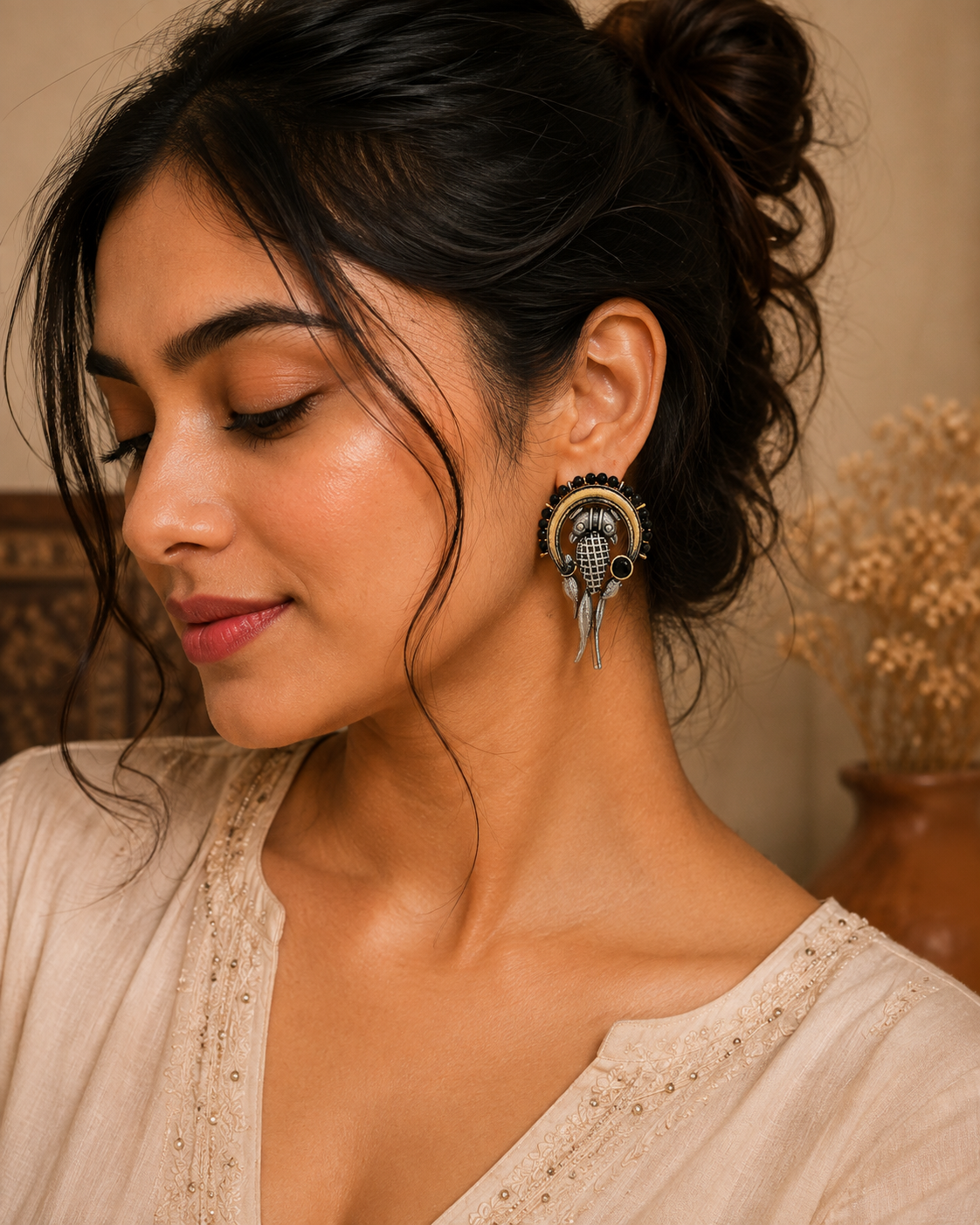 A woman wearing a large, ornate gold and black fish-shaped earring, shown in a close-up portrait against a warm, neutral background.