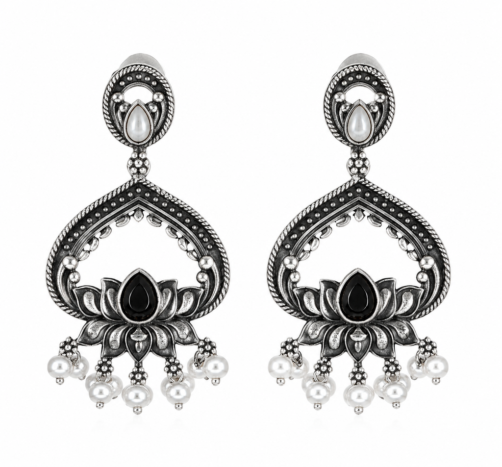 A pair of ornate silver-toned dangle earrings with black oxidized detailing, featuring lotus motifs, teardrop-shaped black stones, and small dangling pearl-like beads on a plain white background.