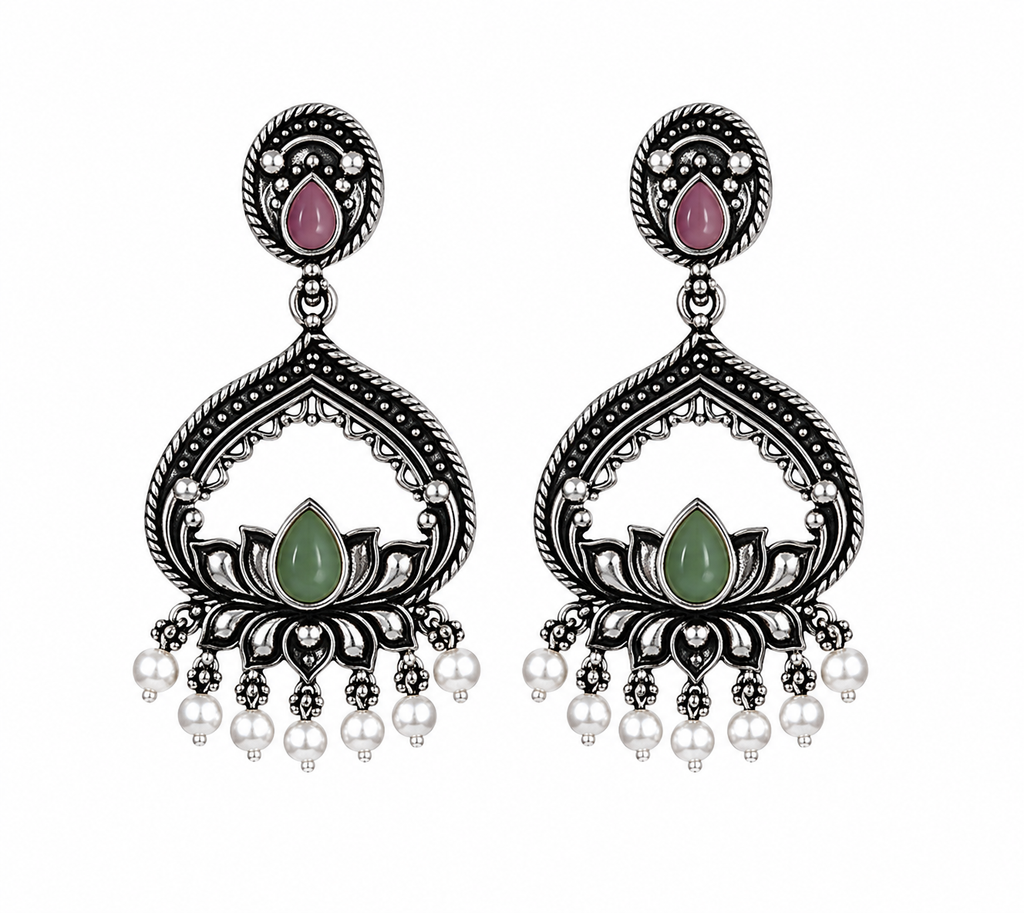 A pair of silver-toned Indian chandelier earrings featuring a pink teardrop stone at the top, a green lotus flower centerpiece, and dangling white pearl beads, shown on a plain white background.